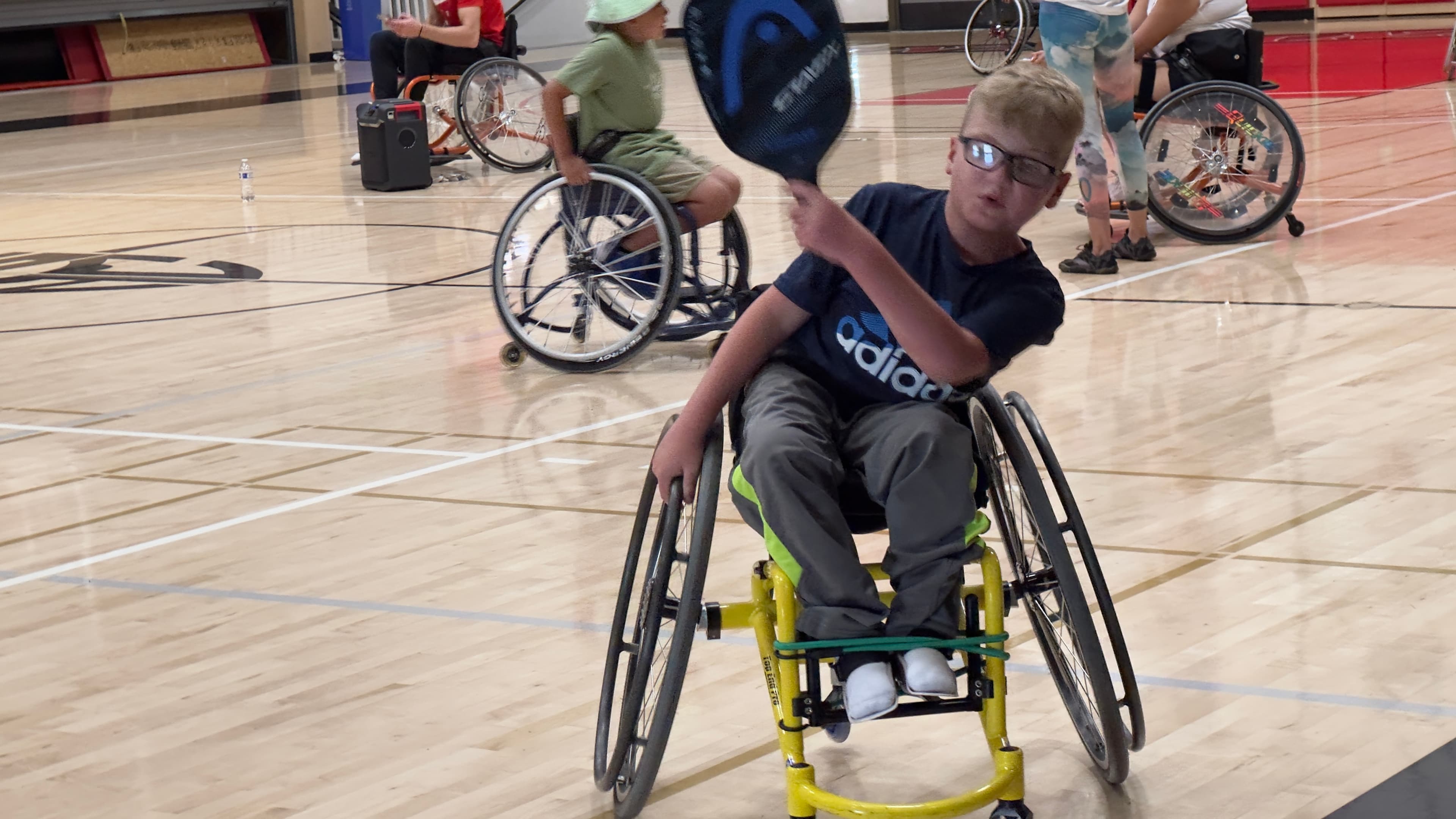 A wheelchair athlete reaches high for an overhead in an indoor match.