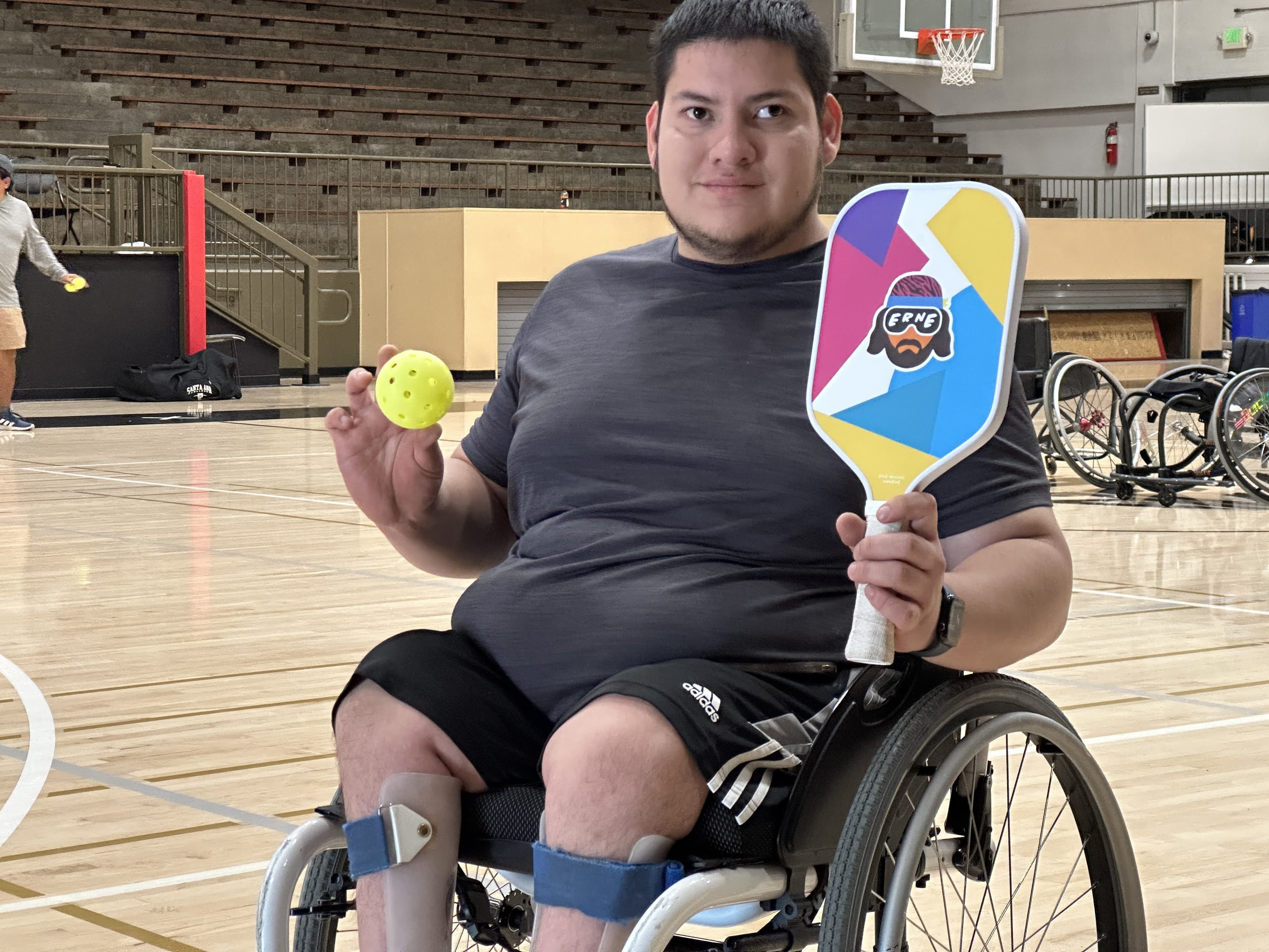 A wheelchair athlete holds up his paddle and ball with a proud smile.