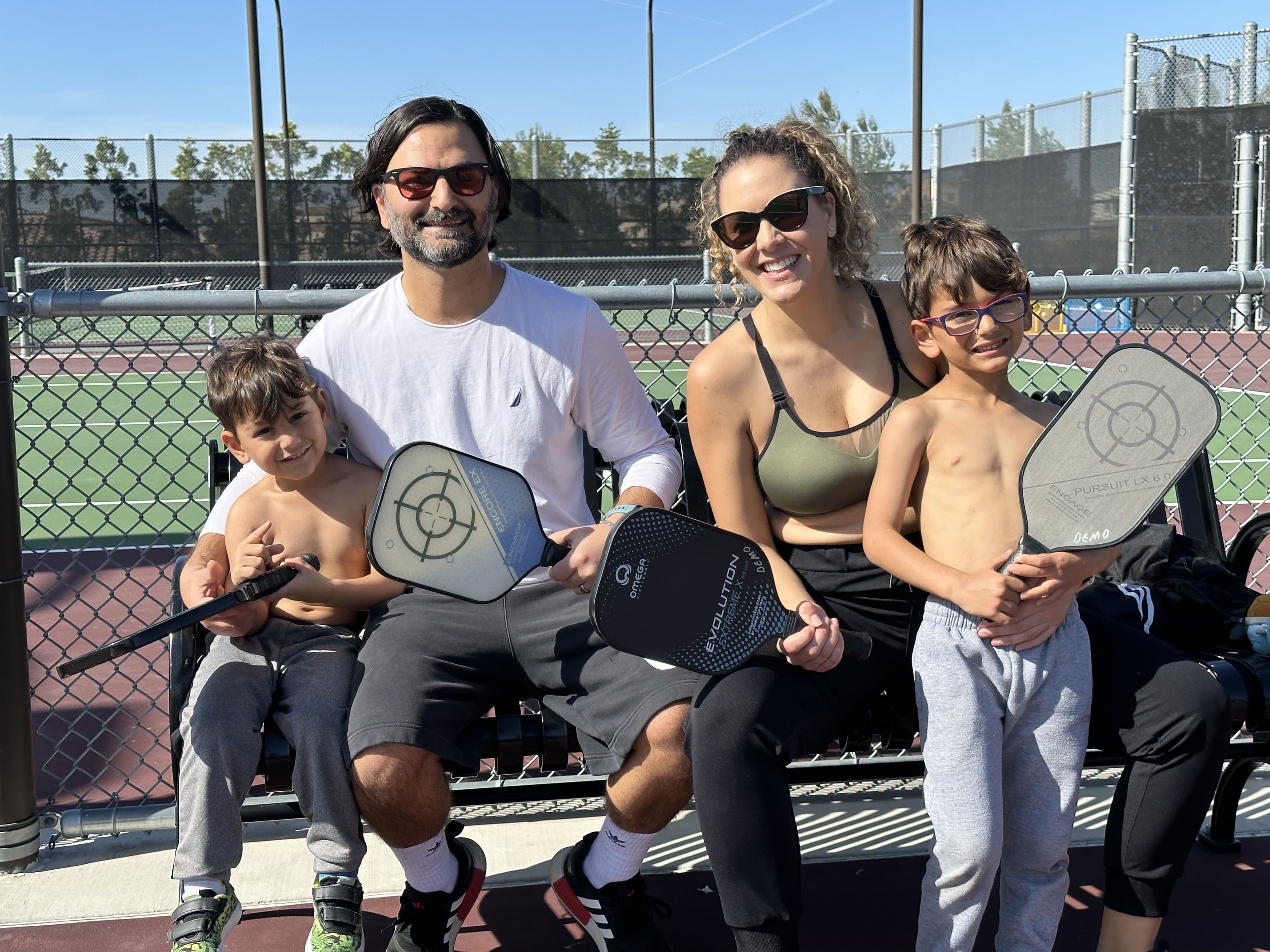 A family beams together on court, each holding a paddle.