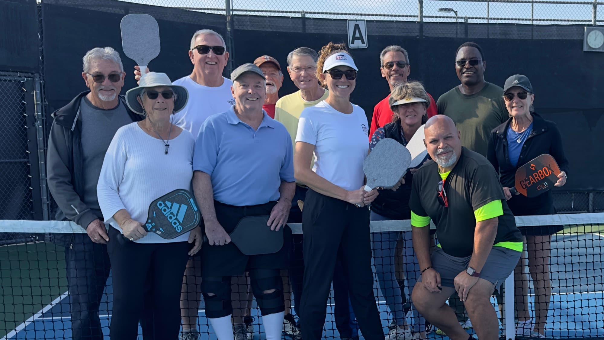 The Lab crew — a dozen players with paddles up, gathered at the net after a session.