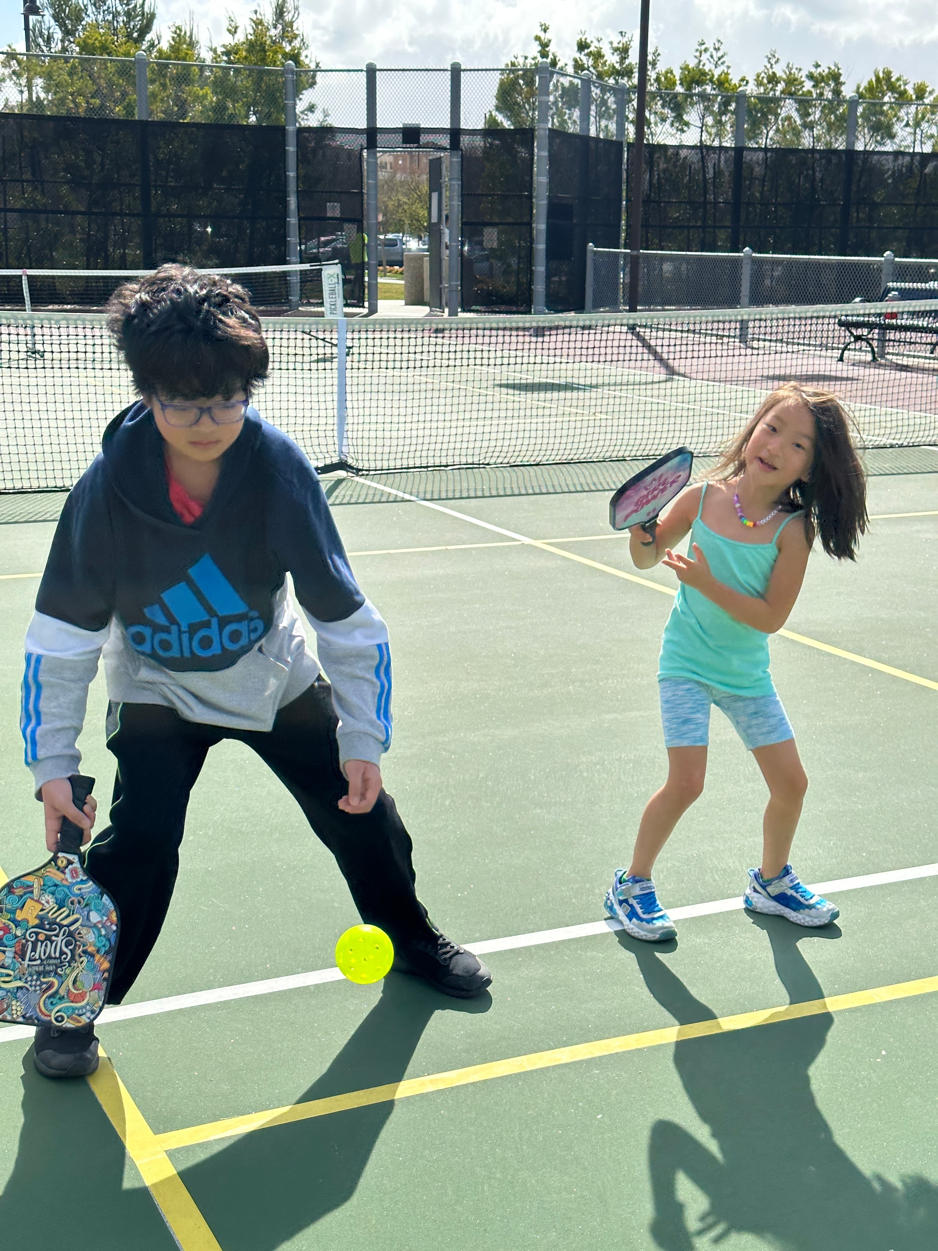 A coach and a young player rally together on a sunny court.