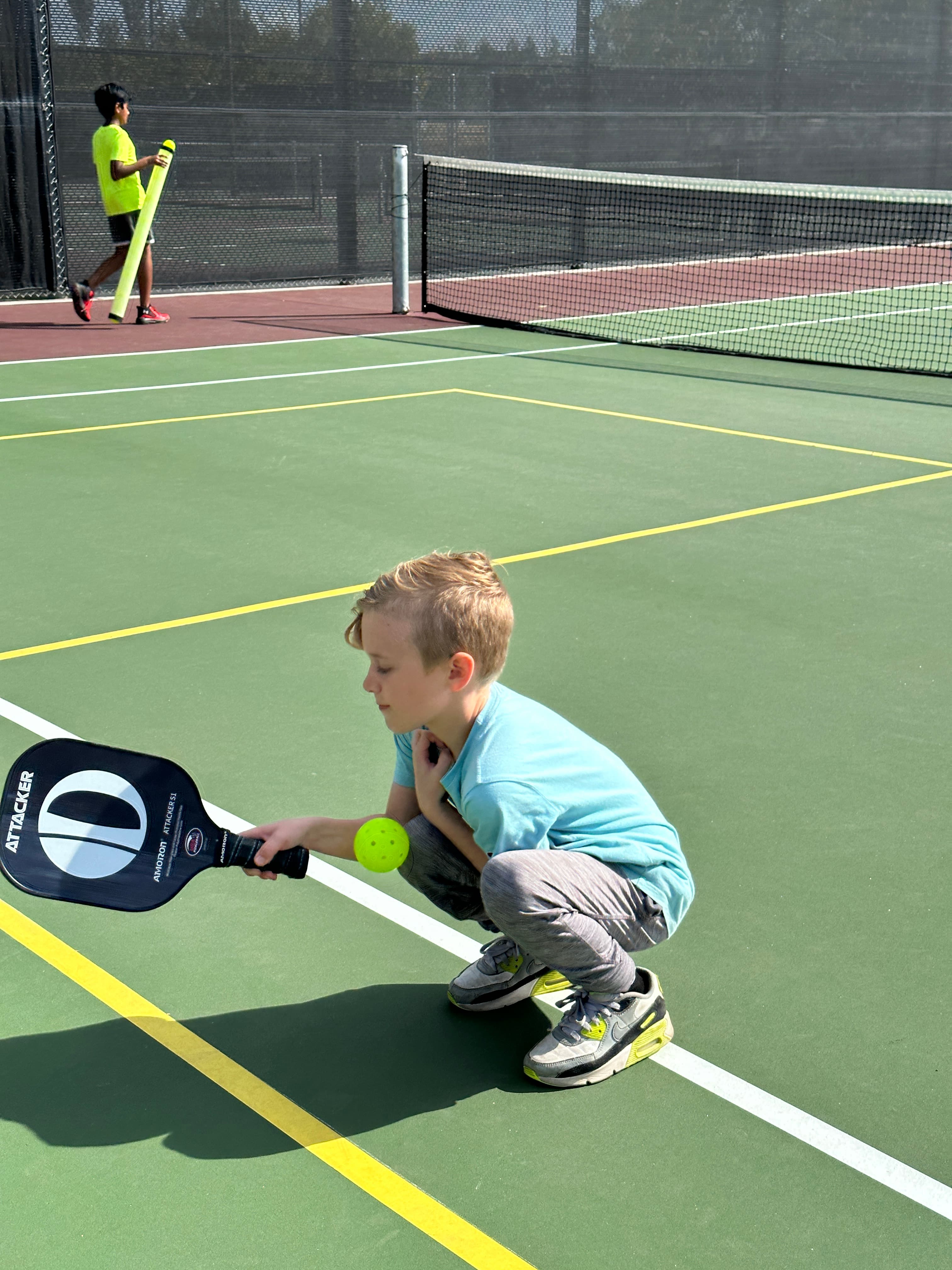 A young player scoops a low ball with focus and a big grin.